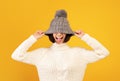 Playful millennial woman pulling down woollen hat and sticking out her tongue, fooling over yellow background Royalty Free Stock Photo