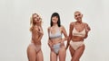 Playful mood. Three happy mature women in underwear posing together half naked isolated over light background, smiling Royalty Free Stock Photo