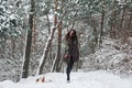 Playful mood. Woman in warm clothes walks the dog in the snowy forest. Front view Royalty Free Stock Photo