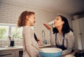 Playful mother and daughter preparing food while playing with flour in modern kitchen at home