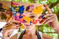 Playful portrait of a young gorgeous female artist painter covered in paint, looking and smiling at camera. Creativity concept.