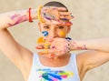 Playful portrait of a young gorgeous female painter artist, with hands covered in paint, looking and smiling at camera. Royalty Free Stock Photo