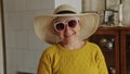 playful and pretty senior Caucasian woman with pink sunglasses and a hat smiling happily medium closeup indoor seniority