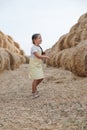 Playful shining little braided girl running on hay country field road between haystacks looking away in sundress. Having