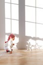 Playful small child wears santa hat, plays with artificial snow in spacious room, looks attentively star, has dreamy and