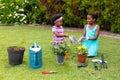 Playful smiling african american sisters kneeling while wearing gloves by plants in garden