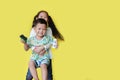 Playful of smiling asian sister hugging and lift up her happy little brother standing on yellow background with copy space Royalty Free Stock Photo