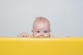 Playful surprised baby peeking out of playpen. Happy childhood