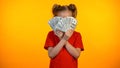 Playful teenage girl closing face with dollar banknotes, happy with first income