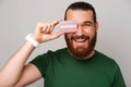 Playful young bearded man covers on eye with a red credit card while smiling.