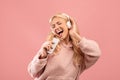 Playful young lady singing and holding smartphone like microphone wearing wireless headphones, pink background Royalty Free Stock Photo