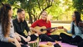 Playful young people are singing and moving hands when beautiful girl is playing the guitar during picnic in park on Royalty Free Stock Photo