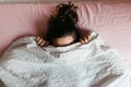 Playful young woman hiding face under blanket while lying in cozy bed on white pillow, pretty curious girl feeling shy peeking Royalty Free Stock Photo