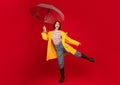 Playful young woman holding umbrella and having fun, laughing and looking at camera over red studio background Royalty Free Stock Photo