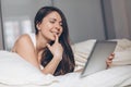 Playful young woman with tablet in hands on bed at home