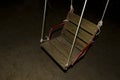 Playground at night, spooky photo. Backlit wooden swing. Isolation, loneliness and sadness concept