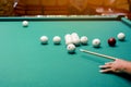 Playing billiards, close up of a mans hand with a cue hitting a white ball. Balls with numbers on green billiard table Royalty Free Stock Photo