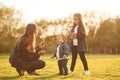 Illuminated by sunlight. Playing with dandelion. Woman with her two young daughters is on the summer field