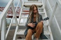 Playing a guitalele cute teenager girl with dreads sitting on a steel stairs