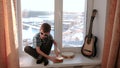 Playing a musical instrument. Boy plays the drum sitting on the windowsill slomo