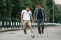 Playing with soccer ball. Two men with crutches is outdoors on the road Royalty Free Stock Photo