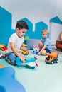 Playtime at nursery school. Toddlers boys sitting on the floor and playing with colorful plastic cars, boats, planes and Royalty Free Stock Photo