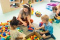 Playtime at nursery school. Toddlers with their teacher sitting on the floor and playing with building blocks, colorful Royalty Free Stock Photo