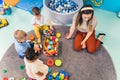 Playtime at nursery school. Toddlers with their teacher sitting on the floor and playing with building blocks, colorful Royalty Free Stock Photo