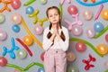 Pleading child. Sad upset little girl with pigtails standing against gray wall decorated with colorful balloons keeps hands in Royalty Free Stock Photo