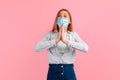 Pleading woman, wearing a medical protective mask on her face, prays with her hands clasped in prayer against a pink background Royalty Free Stock Photo