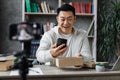 Pleasant asian man opening parcel box with new smartphone