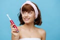 a pleasant, beautiful young woman stands on a blue background in a towel, holding a red toothbrush in her hand, smiling Royalty Free Stock Photo