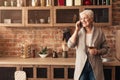 Relaxed Aged Lady With Cellphone And Wine Glass In Kitchen Interior