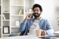 Pleasant Call. Smiling Handsome Indian Man Talking On Cellphone And Drinking Coffee Royalty Free Stock Photo