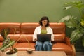 Pleasant caucasian young girl uses laptop sitting on sofa indoors. Royalty Free Stock Photo