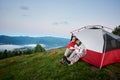 Pleasant couple hugging sit in tent against landscape of mighty Carpathian mountains