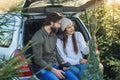 Pleasant couple sitting in car trunk and looking at wonderful christmas tree they choose for holidays at plantings area.