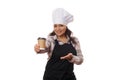 Pleasant female bartender waitress wearing chef hat and black apron, holding out hot drink to go, smiling on camera