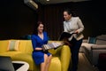 Pleasant female sales manager, interior designer presenting samples of fabrics for sofas to a woman customer, sitting on a yellow Royalty Free Stock Photo