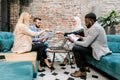 Pleasant four diverse multiethnic young business people, men and women, sitting on the soft sofa in the modern office Royalty Free Stock Photo