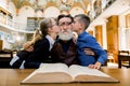 Pleasant handsome bearded old grandfather spending time in the library with his granddaughter and grandson, kissing him