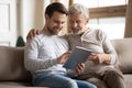 Grownup son teaching elderly mature father using applications on tablet.