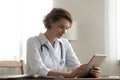 Pleasant happy female doctor general practitioner using digital computer tablet.