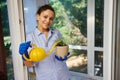 Pleasant housewife in blue gloves smiles looking at camera while watering a potted rosemary plant with a watering can