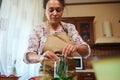 Pleasant housewife putting chili peppers into a sterilized glass can while canning in the home kitchen.