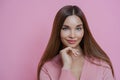 Pleasant looking brunette female fashion model keeps hand under chin, has full lips and applealing appearance, wears rosy jumper