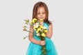 Pleasant looking kid with dark straight hair, focused down on flowers, wears poofy blue dress, isolated over white background,