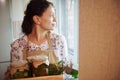 Pleasant looking through the window, holding box with jars of pickled vegetables, preserved according to homemade recipe