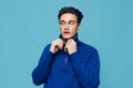 pleasant man stands in a blue zip-up sweater adjusting the collar, smiling pleasantly looking away. Studio photo on a Royalty Free Stock Photo