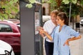 Pleasant middle aged woman helping young girl to buy ticket for street parking in modern parking meter Royalty Free Stock Photo